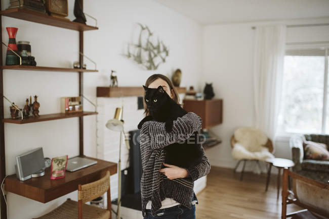 Chica sosteniendo gato negro en sala de estar - foto de stock