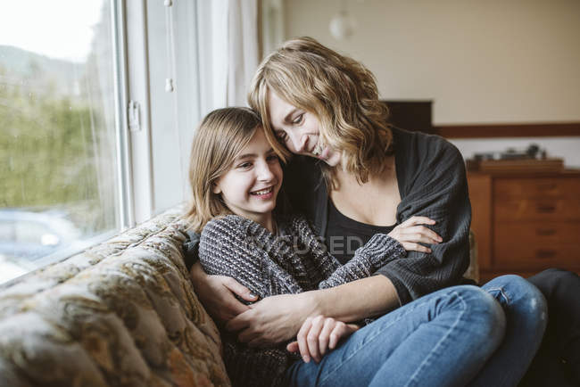 Cariñosa madre e hija abrazándose en el sofá de la sala de estar - foto de stock