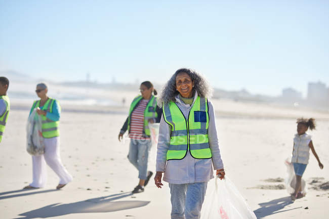 Retrato confiado mujer mayor voluntaria limpieza de basura en la playa soleada - foto de stock