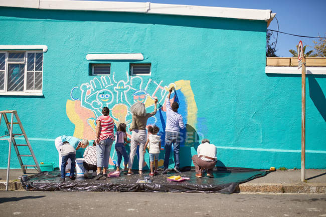 Community volunteers painting vibrant mural on sunny urban wall — Stock Photo