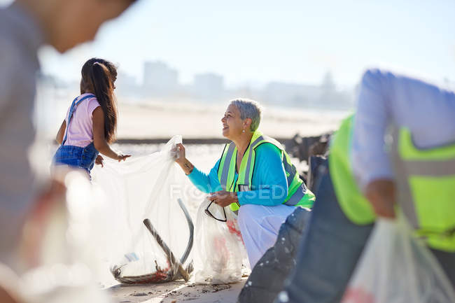 Senior mulher e menina voluntária limpeza litter na praia ensolarada — Fotografia de Stock