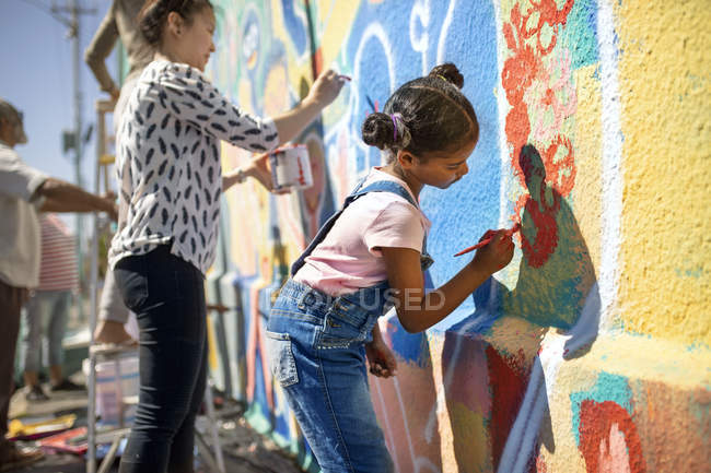 Chica voluntaria pintura vibrante mural en la pared soleada - foto de stock
