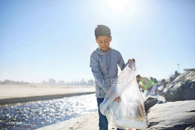 Niño voluntario limpieza de basura en la playa soleada - foto de stock