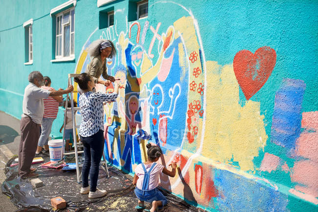 Общественные волонтеры рисуют многоцветные фрески на солнечной городской стене — стоковое фото