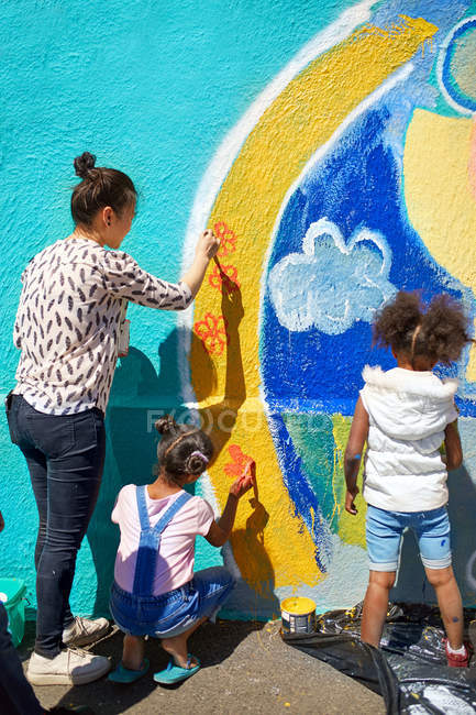 Mãe e filha voluntários pintando mural vibrante na parede ensolarada — Fotografia de Stock