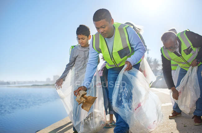 Hombres de familia multi-generación voluntarios, recogiendo basura en muelle frente al mar - foto de stock