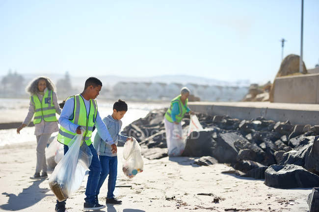 Padre e hijo voluntarios limpiando basura en la playa soleada - foto de stock