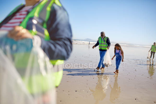 Grandfather and granddaughter volunteers cleaning up litter on sunny wet sand beach — Stock Photo