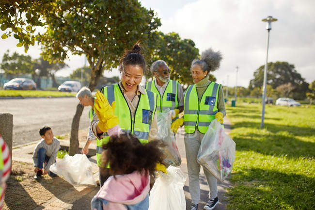 Voluntarios felices chocando los cinco, limpiando basura en el soleado parque - foto de stock