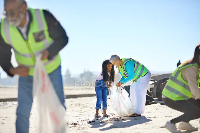 Senior mulher e menina voluntária limpeza litter em ensolarado, praia de areia — Fotografia de Stock