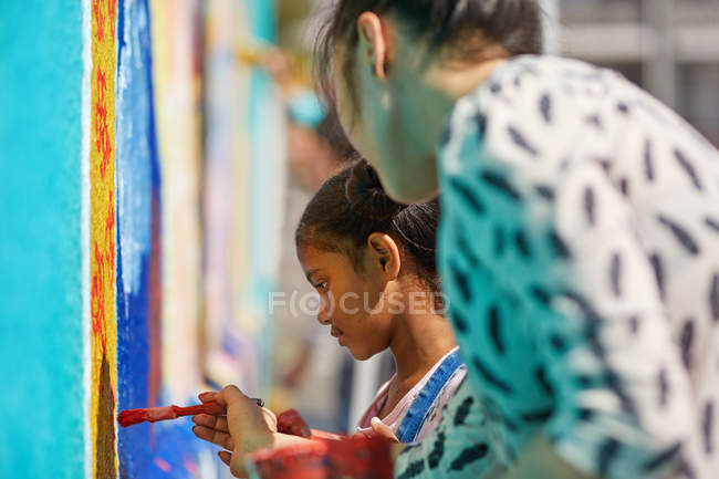 Professor e elementar menina estudante pintura na parede — Fotografia de Stock