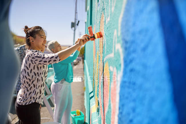 Женщины рисуют яркие фрески на солнечной городской стене — стоковое фото