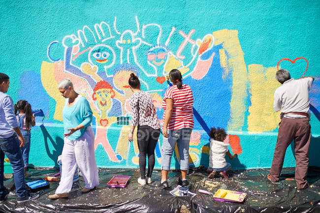 Voluntários comunitários pintando mural vibrante na parede ensolarada — Fotografia de Stock