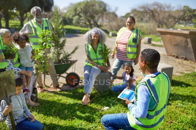 Человек с цифровыми планшетами ведущих волонтеров посадки деревьев в солнечном парке — стоковое фото