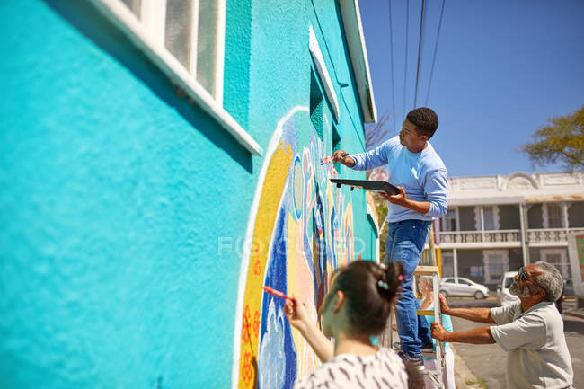 Voluntários comunitários pintando mural vibrante na parede urbana ensolarada — Fotografia de Stock