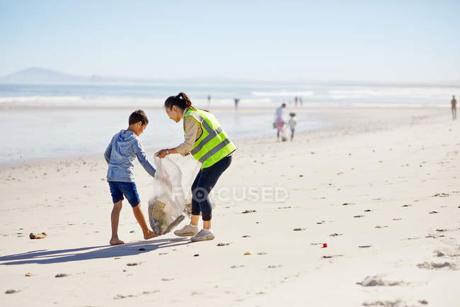 Mother and son volunteers cleaning up litter on sunny, sandy beach — Stock Photo