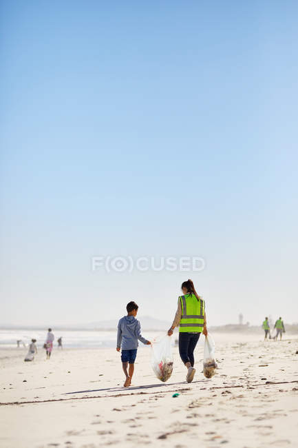 Mère et fils bénévoles nettoient la litière sur une plage ensoleillée et sablonneuse — Photo de stock