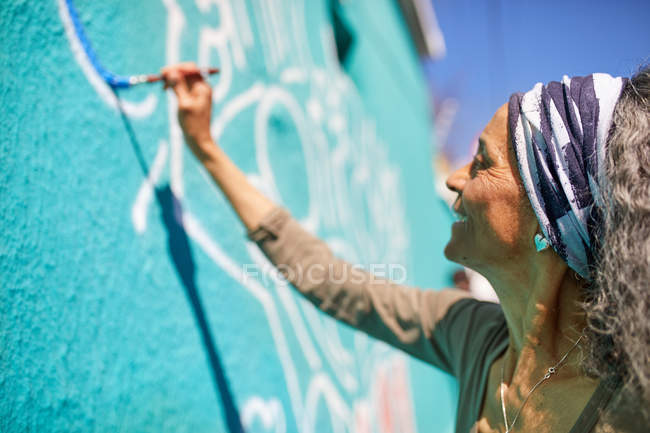 Старшая женщина рисует фрески на солнечной стене — стоковое фото