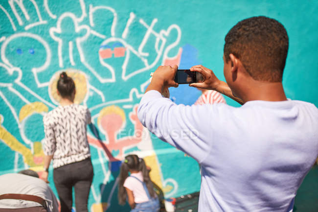 Man with camera phone photographing community mural on sunny wall — Stock Photo