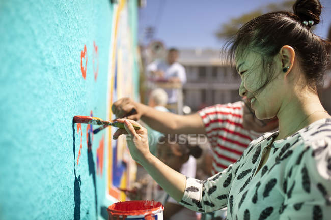 Lächelnde Ehrenamtliche malen Wandbild an sonniger Wand — Stockfoto