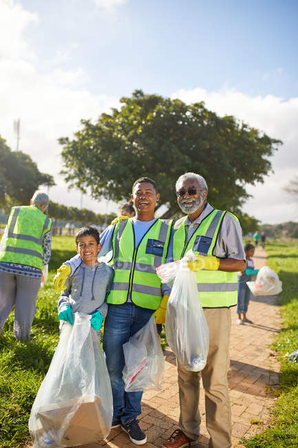 Portrait happy multi-generation men volunteering, cleaning up litter in sunny park — Stock Photo