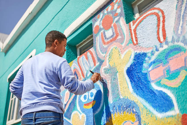 Мужчина-волонтер рисует яркую фреску на солнечной стене — стоковое фото