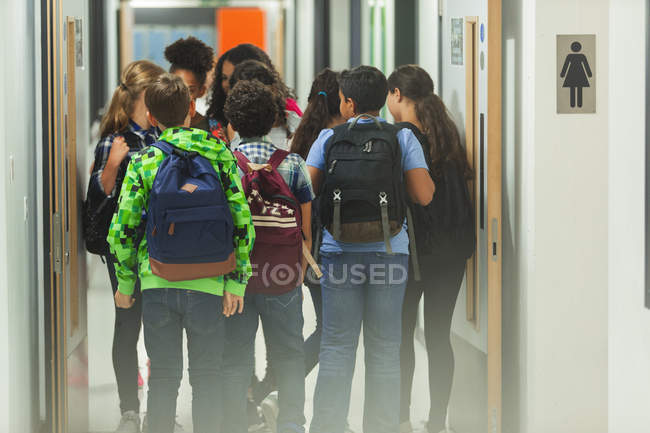 Estudiantes de secundaria con mochilas caminando en el pasillo de la escuela - foto de stock