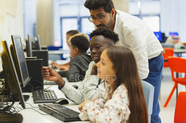 Enseignant aidant les étudiants du premier cycle du secondaire à utiliser l'ordinateur dans un laboratoire informatique — Photo de stock