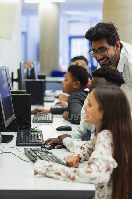 Profesor ayudando a estudiantes de secundaria a usar la computadora en el laboratorio de computación - foto de stock