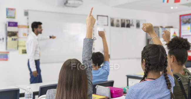 Junior high school students with hands raised during lesson in classroom — Stock Photo