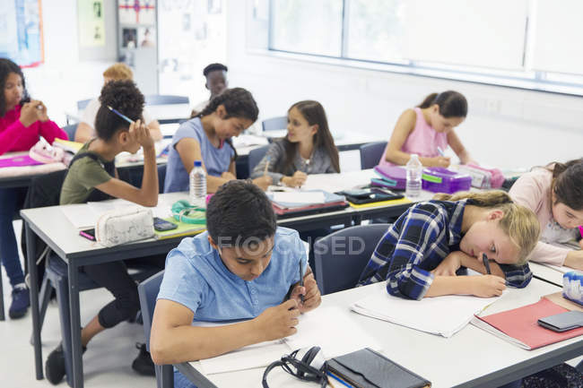Studenti delle scuole medie che studiano alle scrivanie in classe — Foto stock