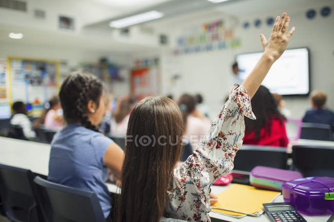 Junior high school girl student with hand raised in classroom — Stock Photo