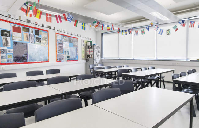 International flags hanging over desks in classroom — Stock Photo