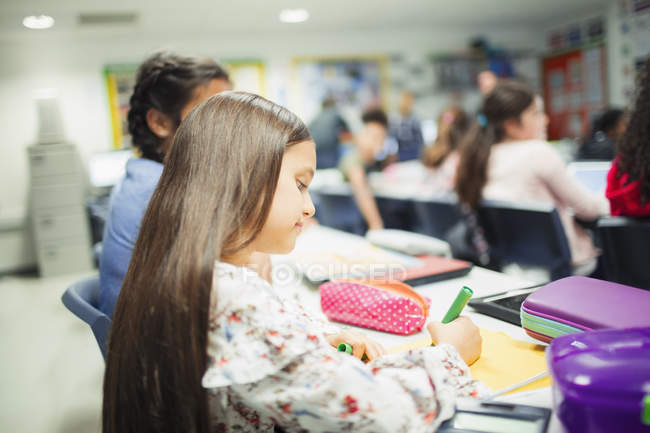 Junior high school girl student doing homework at desk in classroom — Stock Photo
