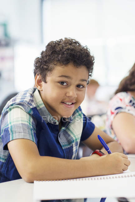 Retrato de menino de idade elementar confiante fazendo lição de casa em sala de aula — Fotografia de Stock