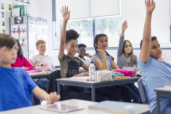 Junior high school students with hands raised in classroom — Stock Photo