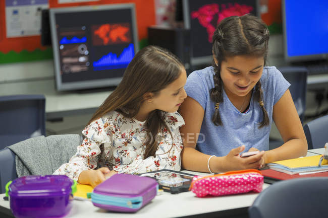 Молодші школярі використовують смартфон за столом у класі — стокове фото