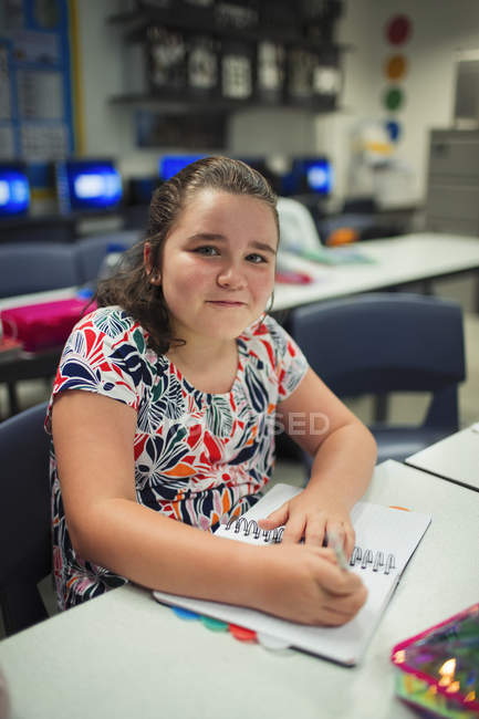 Porträt einer lächelnden, selbstbewussten Realschülerin, die im Klassenzimmer in ein Notizbuch schreibt — Stockfoto