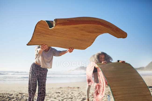 Mulher que coloca tapetes de ioga na praia ensolarada durante retiro de ioga — Fotografia de Stock