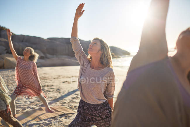 Спокойная женщина практикует позу воина наоборот на солнечном пляже во время йоги отступления — стоковое фото