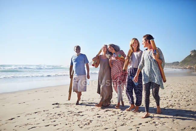 Amigos andando com tapetes de ioga na praia ensolarada durante retiro de ioga — Fotografia de Stock