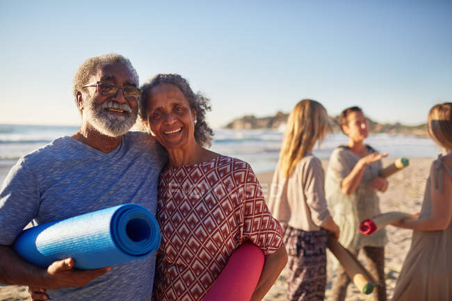 Portrait happy senior couple with yoga mats on sunny beach during yoga retreat — Stock Photo