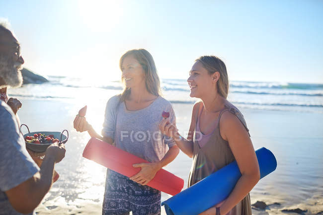 Мати і дочка з йога килимками їдять свіжі ягоди на сонячному пляжі під час відступу йоги — стокове фото