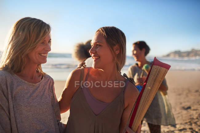 Счастливая мать и дочь с ковриком для йоги на солнечном пляже во время йоги отступления — стоковое фото