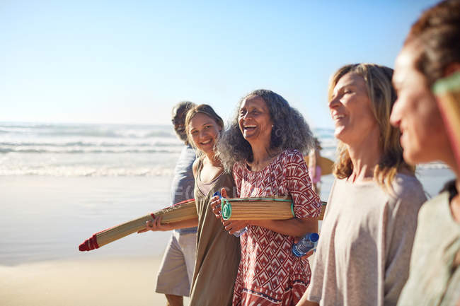 Happy friends with yoga mats on sunny beach during yoga retreat — Stock Photo