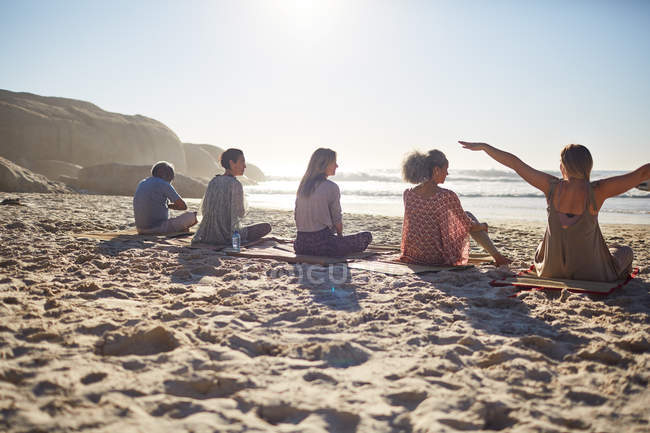 Группа, сидящая на ковриках для йоги на солнечном пляже во время йоги — стоковое фото