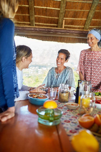 Happy friends enjoying healthy breakfast in hut during yoga retreat — Stock Photo