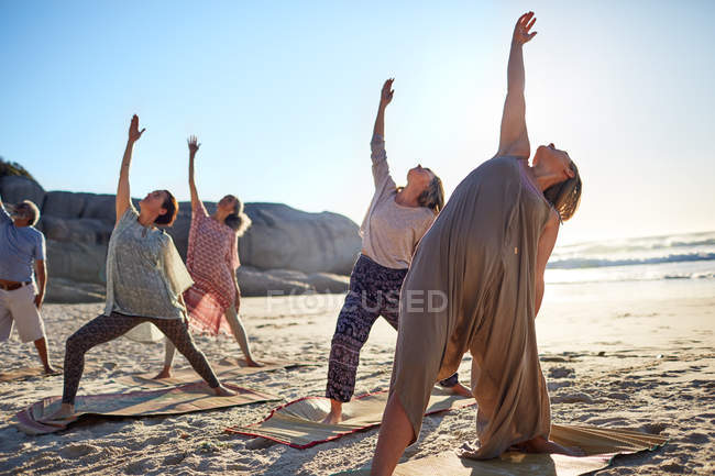 Group practicing yoga reverse warrior pose on sunny beach during yoga retreat — Stock Photo