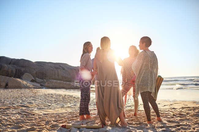 Женщины, стоящие в кругу на солнечном пляже во время йоги отступления — стоковое фото