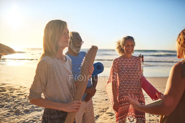 Smiling friends with yoga mats on sunny beach during yoga retreat — Stock Photo